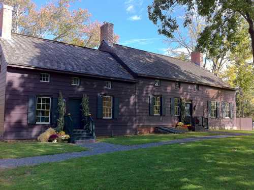 A historic brown wooden house with green shutters, surrounded by a lawn and seasonal decorations.