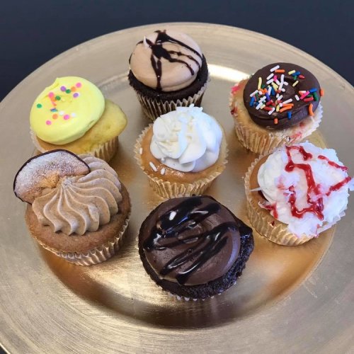 A variety of colorful cupcakes on a gold plate, featuring different toppings and flavors.