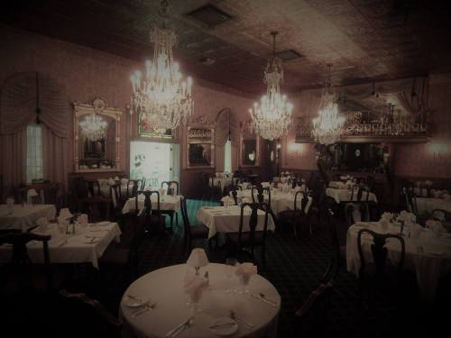 Elegant dining room with chandeliers, round tables set with white linens, and a vintage decor ambiance.