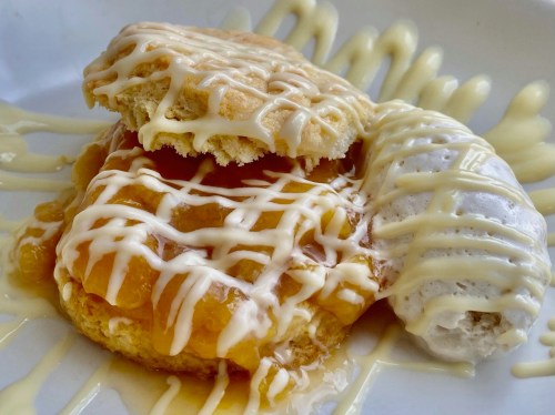 A close-up of a dessert featuring a biscuit topped with peach filling and drizzled with white icing.