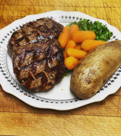 Grilled steak with carrots, lettuce, and a baked potato on a decorative plate.
