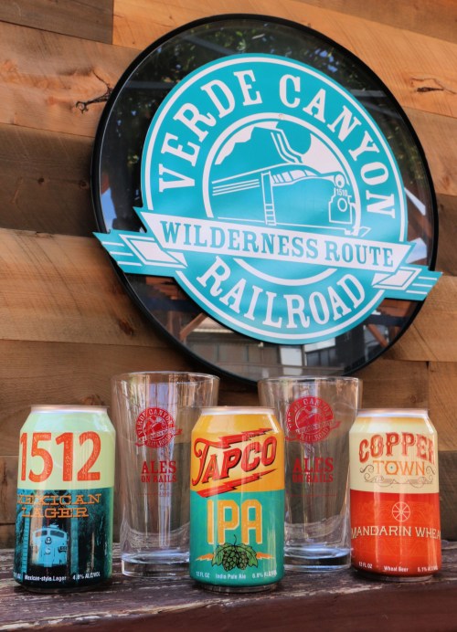 A display featuring Verde Canyon Railroad sign, craft beer cans, and glasses on a wooden background.