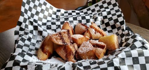 A basket of golden, triangular pastries dusted with powdered sugar on a black and white checkered paper.