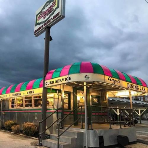 A colorful diner with a pink and green awning, featuring a sign for curb service and outdoor seating.