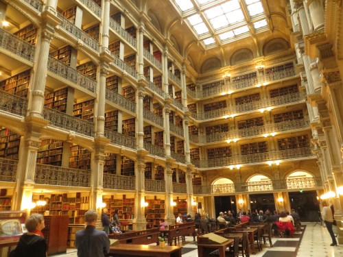 A grand library interior with tall bookshelves, ornate architecture, and people reading at wooden tables.