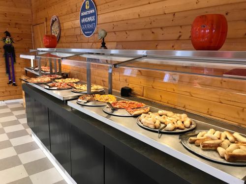A buffet display of various pizzas and breadsticks on trays in a wooden interior setting.