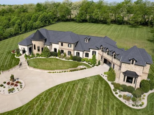 Aerial view of a large, elegant stone house surrounded by manicured lawns and trees.