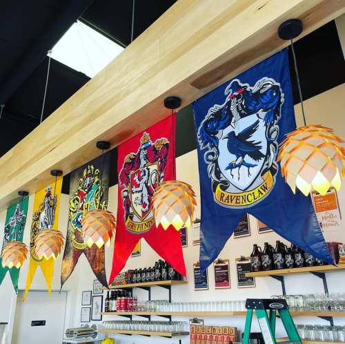 Banners of four Hogwarts houses hang from a wooden beam, with unique pendant lights illuminating the space below.