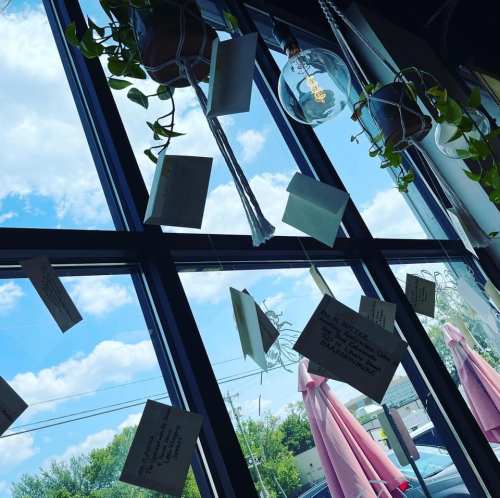 Hanging notes and plants near a window, with a blue sky and clouds visible outside.