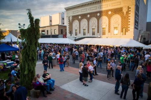 A large crowd gathers at an outdoor event with tents, food stalls, and a historic building in the background.