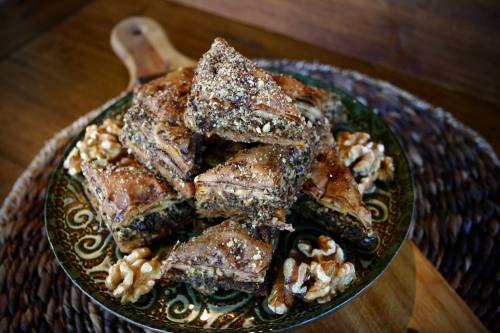 A decorative plate stacked with pieces of baklava, garnished with crushed nuts and surrounded by whole walnuts.
