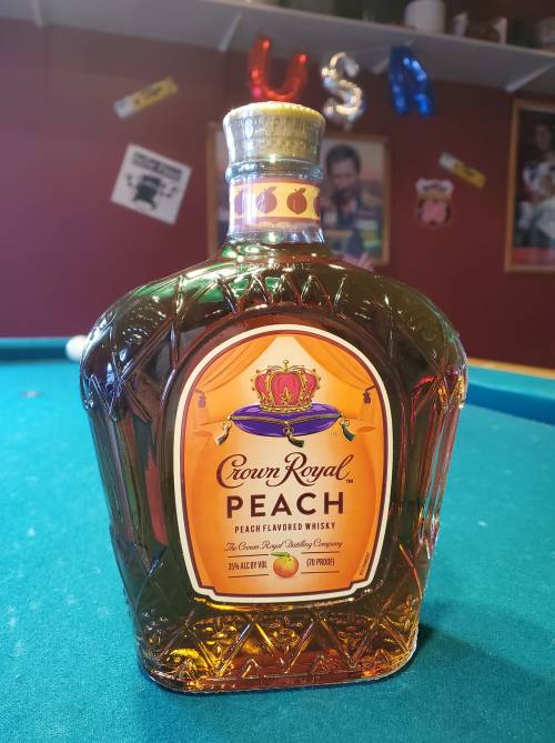 A bottle of Crown Royal Peach flavored whisky on a pool table, with colorful decorations in the background.