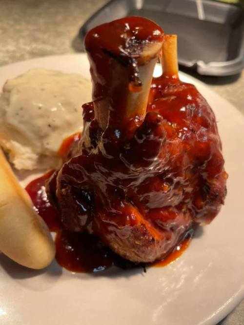 A close-up of a meat dish with barbecue sauce, served with a biscuit and a side of gravy.