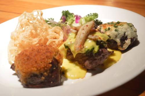 A plate featuring a gourmet meal with meat, creamy sauce, vegetables, and crispy onion strings.
