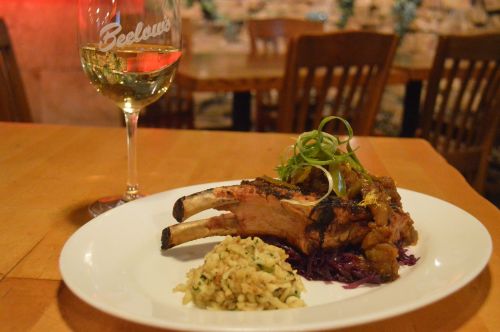 A plate with grilled lamb chops, rice, and purple cabbage, alongside a glass of white wine on a wooden table.