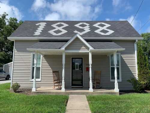 A light-colored house with rocking chairs on the porch and the year "1898" displayed on the roof.