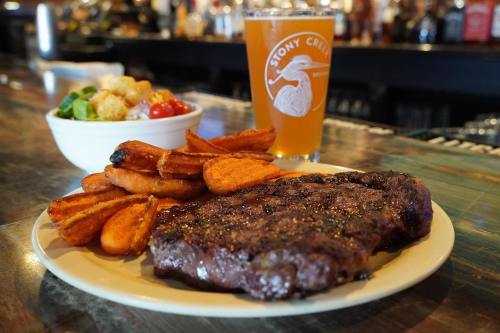 A plate with a grilled steak, sweet potato fries, a salad, and a glass of beer on a bar counter.