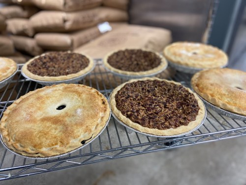 A variety of freshly baked pies cooling on a wire rack, with bags of flour in the background.
