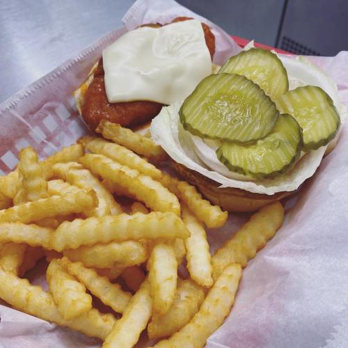 A sandwich with a fried chicken patty, mayonnaise, and pickles, served with crinkle-cut fries on a tray.