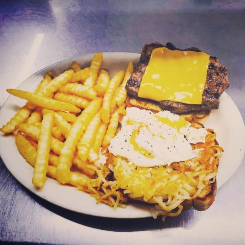 A plate of crinkle-cut fries, a cheeseburger with melted cheese, and a hash brown topped with a poached egg.