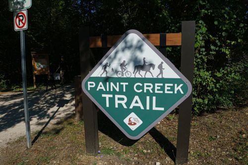 Sign for Paint Creek Trail featuring icons of biking, horseback riding, and hiking, surrounded by trees.