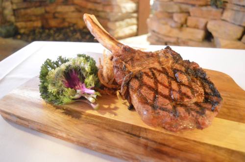 A grilled tomahawk steak on a wooden platter, garnished with a flower and crispy onion strings.