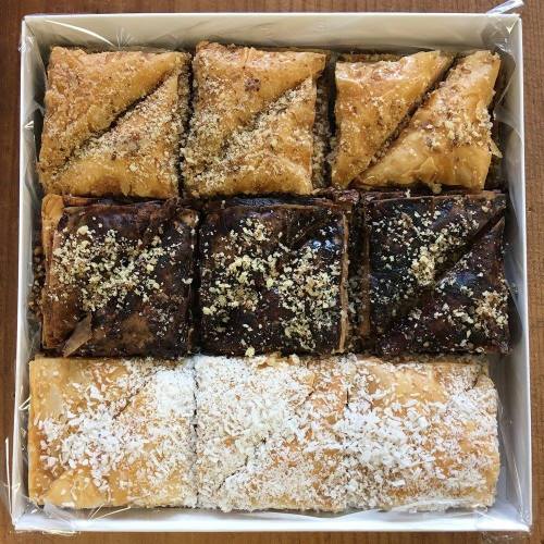 A box of assorted baklava pieces, featuring layers of pastry, nuts, and sweet syrup, topped with coconut and crushed nuts.