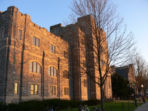 Historic stone building illuminated by sunset, with a bare tree and bicycles in the foreground.