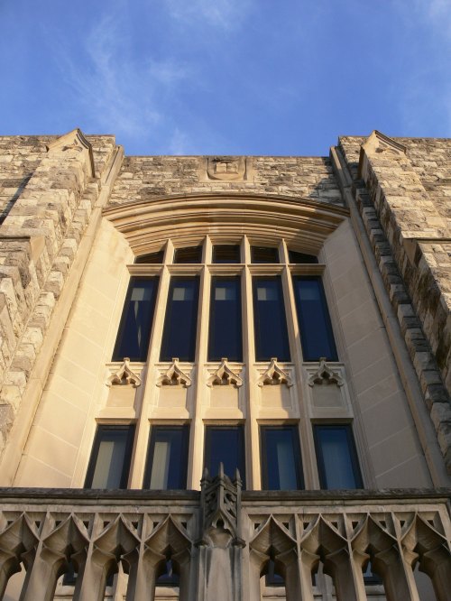 A close-up view of a stone building's ornate window against a blue sky.