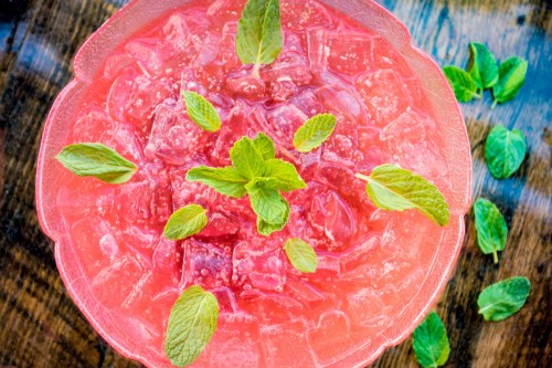 A vibrant pink drink with ice, garnished with fresh mint leaves, served in a decorative bowl on a wooden surface.