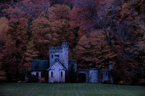 A dark stone castle surrounded by vibrant autumn foliage in a serene landscape.