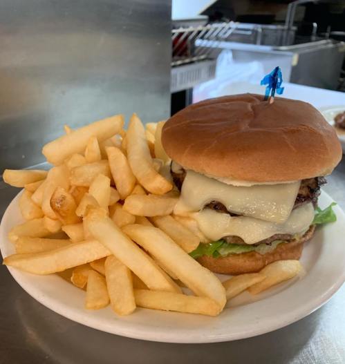 A cheeseburger with melted cheese and lettuce, served with a side of golden French fries on a white plate.