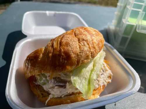 A croissant sandwich filled with chicken salad and lettuce, served in a takeout container.