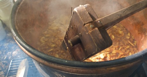 A large pot of simmering food with steam rising, featuring a wooden stirring tool.