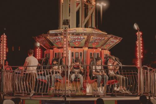 A group of children prepares to ride the Super Shot amusement park attraction at night, surrounded by bright lights.