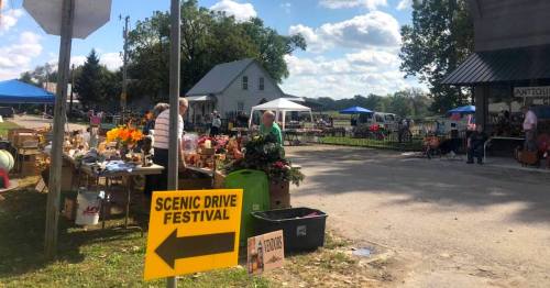 A bustling outdoor festival with vendors, tents, and a sign directing to the Scenic Drive Festival.