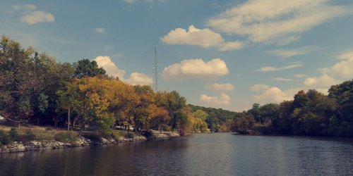 A serene river scene with trees in autumn colors under a blue sky with fluffy clouds.