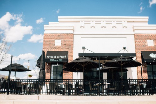 Exterior of a restaurant named "Mad Chef" with outdoor seating, umbrellas, and a clear blue sky.