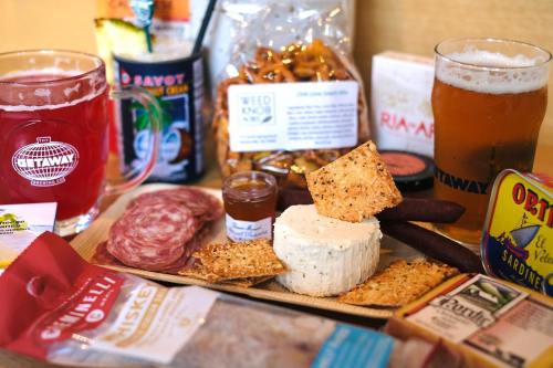 A wooden platter with cheese, crackers, cured meats, and snacks, accompanied by two glasses of beer.