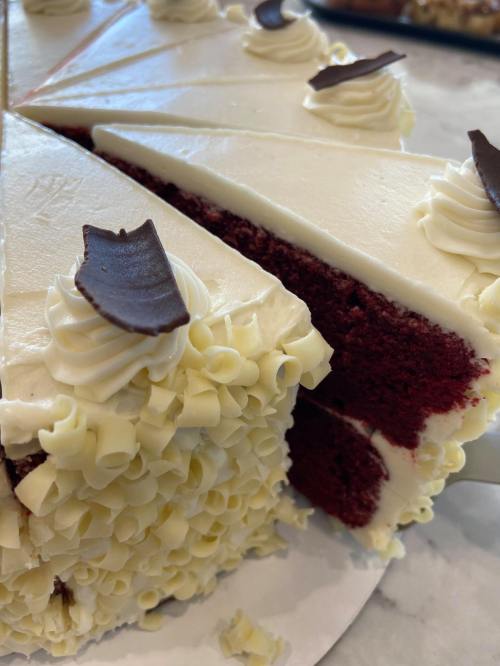 A close-up of a red velvet cake with cream cheese frosting and chocolate decorations, sliced into pieces.