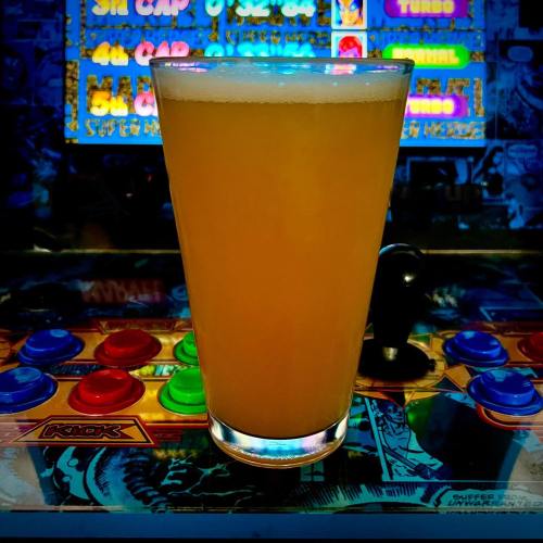 A frosty glass of light-colored beer sits on a colorful arcade game, with vibrant buttons in the foreground.