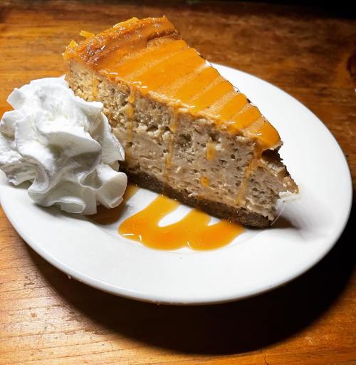 A slice of cheesecake topped with orange glaze, served with a dollop of whipped cream on a white plate.