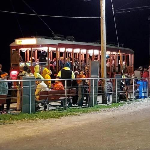 A crowded vintage streetcar at night, with people boarding and waiting on a platform.