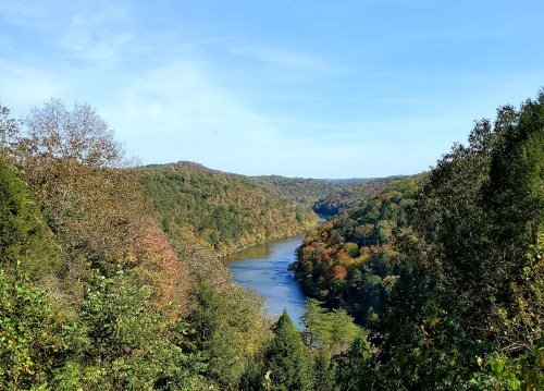 A scenic view of a winding river surrounded by colorful autumn foliage and rolling hills under a clear blue sky.