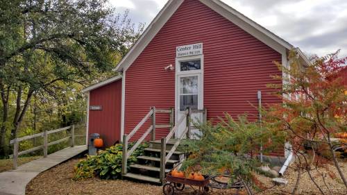 A red building with a sign reading "Center Hill," surrounded by greenery and pumpkins on a path.