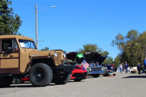 A row of classic cars with open hoods, showcasing their engines, under a clear blue sky.