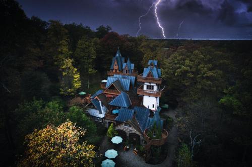 A whimsical castle-like house surrounded by trees, illuminated by lightning in a stormy sky.