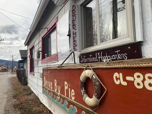 A quaint building with a sign reading "Drive By Pie" and "Order Here," set along a quiet street.