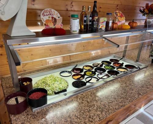 A salad bar with various toppings, including greens, beans, and dressings, set against a wooden backdrop.