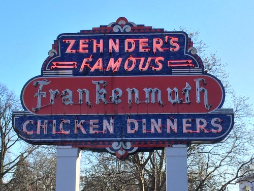 Neon sign for Zehnder's Famous Frankenmuth Chicken Dinners against a clear blue sky.